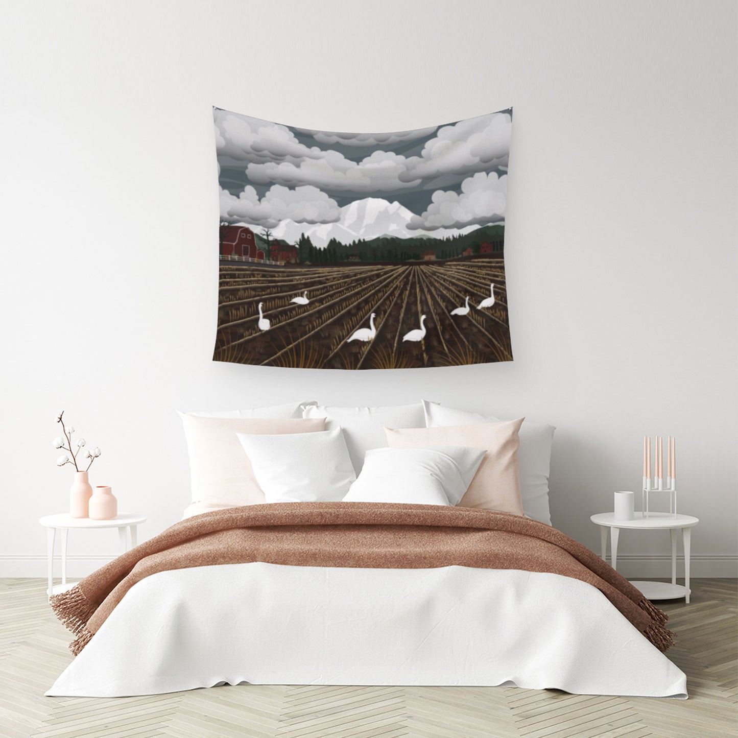 mockup for tapestry with digital design showing Swans frolic in the mud below Mt Baker with clouds over it as a surprised barn watches, the tapestry is above a bed scene with pillows and a few blankets