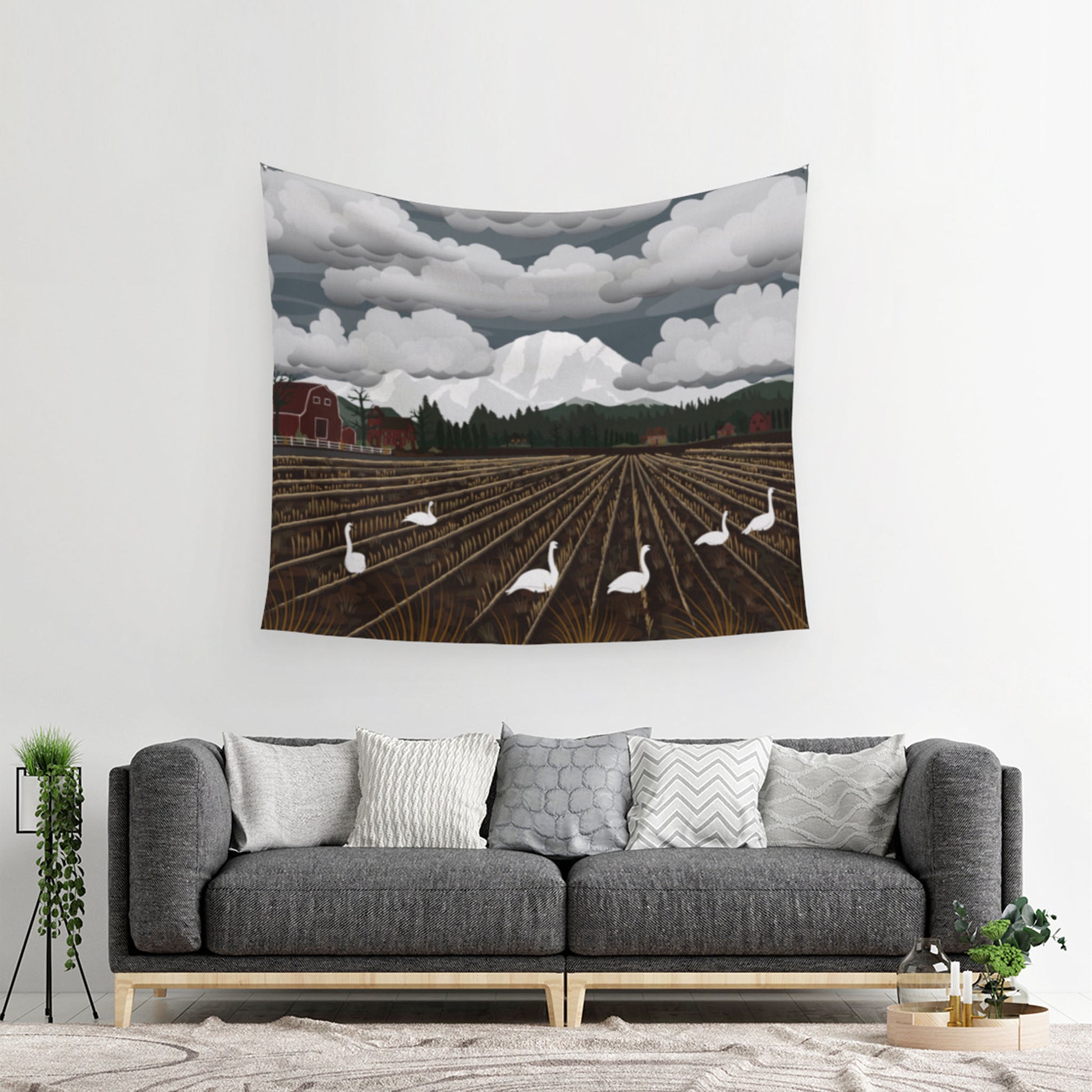 mockup for tapestry with digital design showing Swans frolic in the mud below Mt Baker with clouds over it as a surprised barn watches, the tapestry is above a living room couch that needs a table
