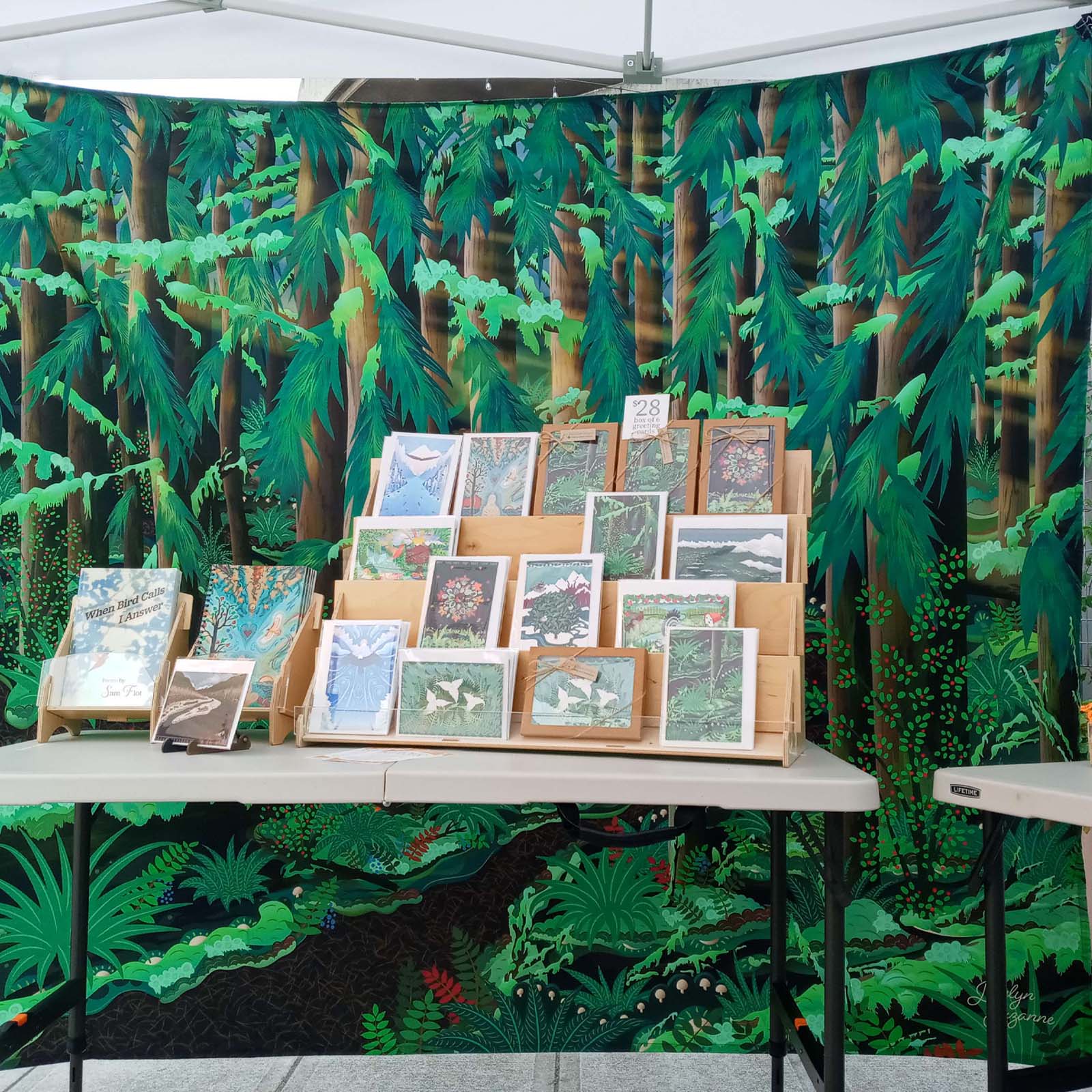 Photo of point of sale shop setup showing our greeting cards on a rack on a table in front of the Loop Trail tapestry as a background for the tent sale